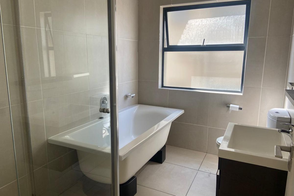 Modern bathroom featuring a freestanding bathtub, glass-enclosed shower, vanity cabinet, and neutral floor-to-ceiling tiling with a top-hung window for natural light.
