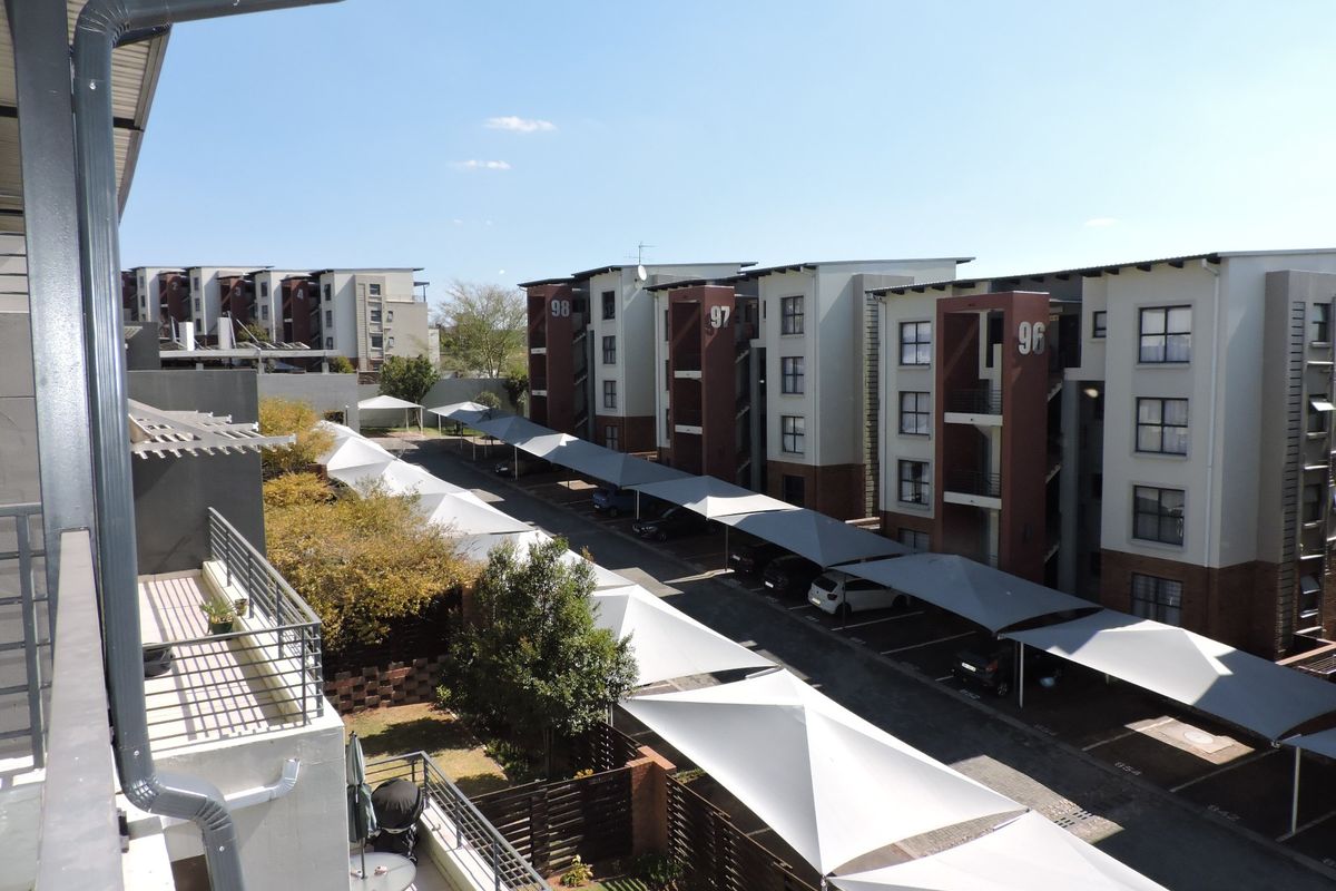 Elevated view of the apartment complex exterior, featuring modern multi-story residential blocks with covered parking bays and landscaped grounds.