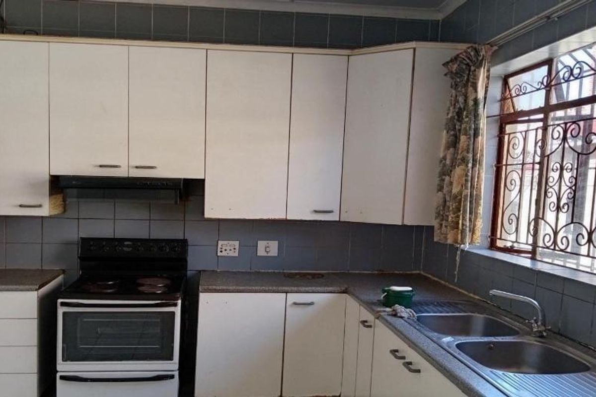 A functional kitchen featuring white cabinetry, a freestanding stove, double bowl sink, and tiled backsplash, requiring cosmetic updates to modernize the space.