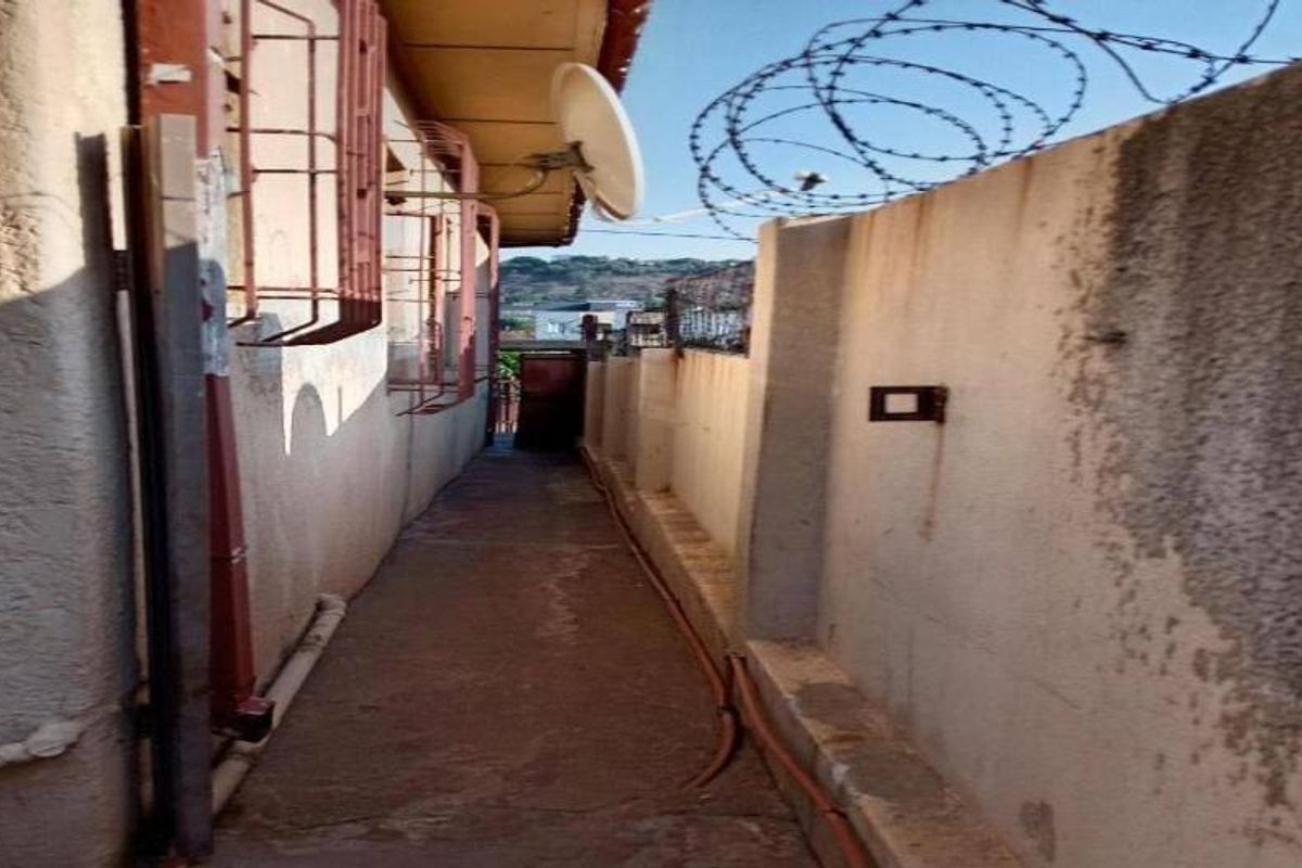 A narrow side passage of the property featuring a concrete walkway, security bars on windows, and a boundary wall topped with razor wire.