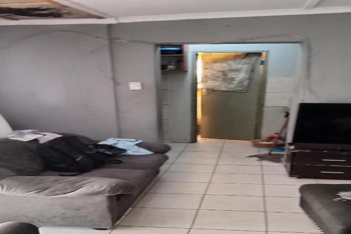 A living room area featuring ceramic floor tiles, showing visible wall cracks and exposed wiring requiring maintenance and cosmetic repair.