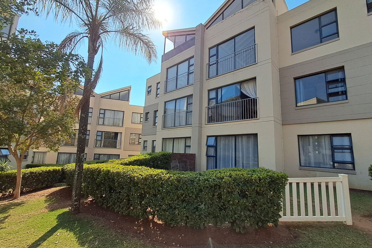 Exterior view of a multi-story apartment complex featuring balconies, aluminium window frames, and a well-maintained garden area with a picket fence.