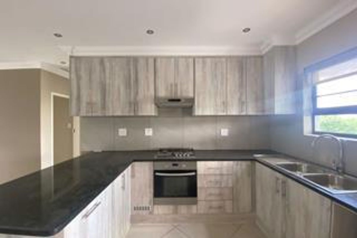 Modern kitchen featuring light wood-grain cabinetry, dark stone countertops, a gas hob, built-in oven, and a double sink with a window view.
