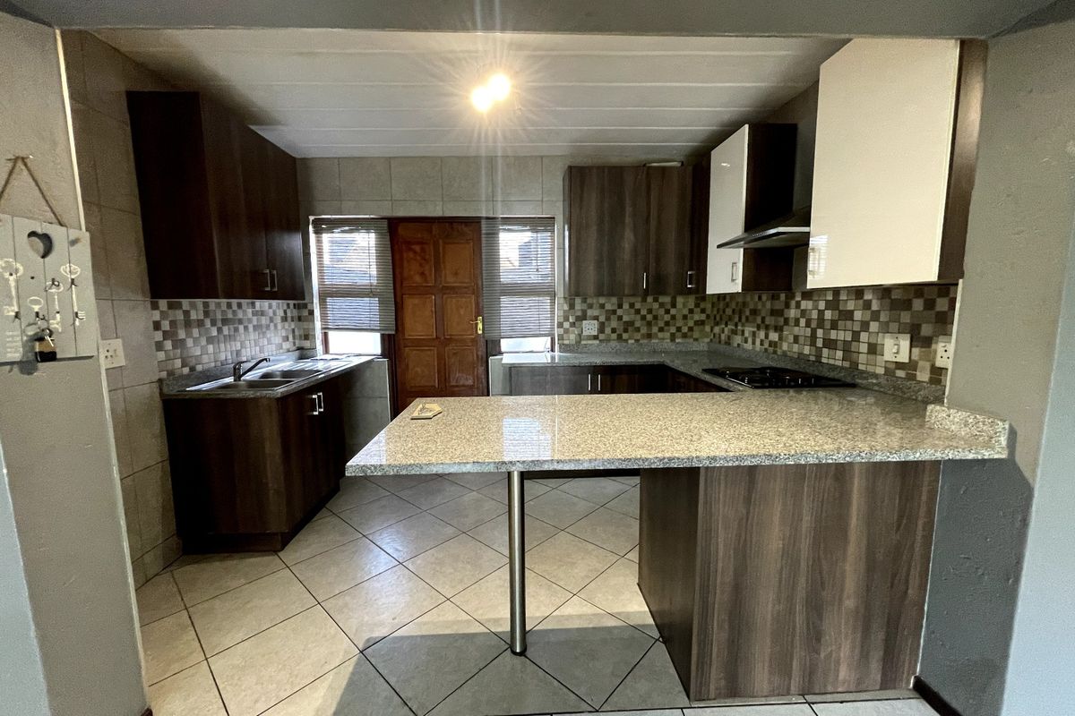 A functional kitchen featuring dark wood cabinetry, granite countertops, a breakfast bar, and tiled finishes throughout.