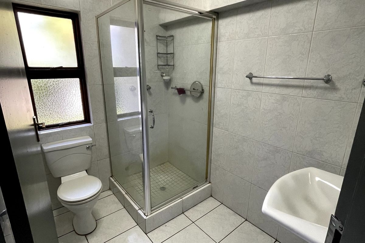 A functional bathroom featuring a pedestal basin, toilet, and a glass-enclosed shower with tiled walls and flooring.