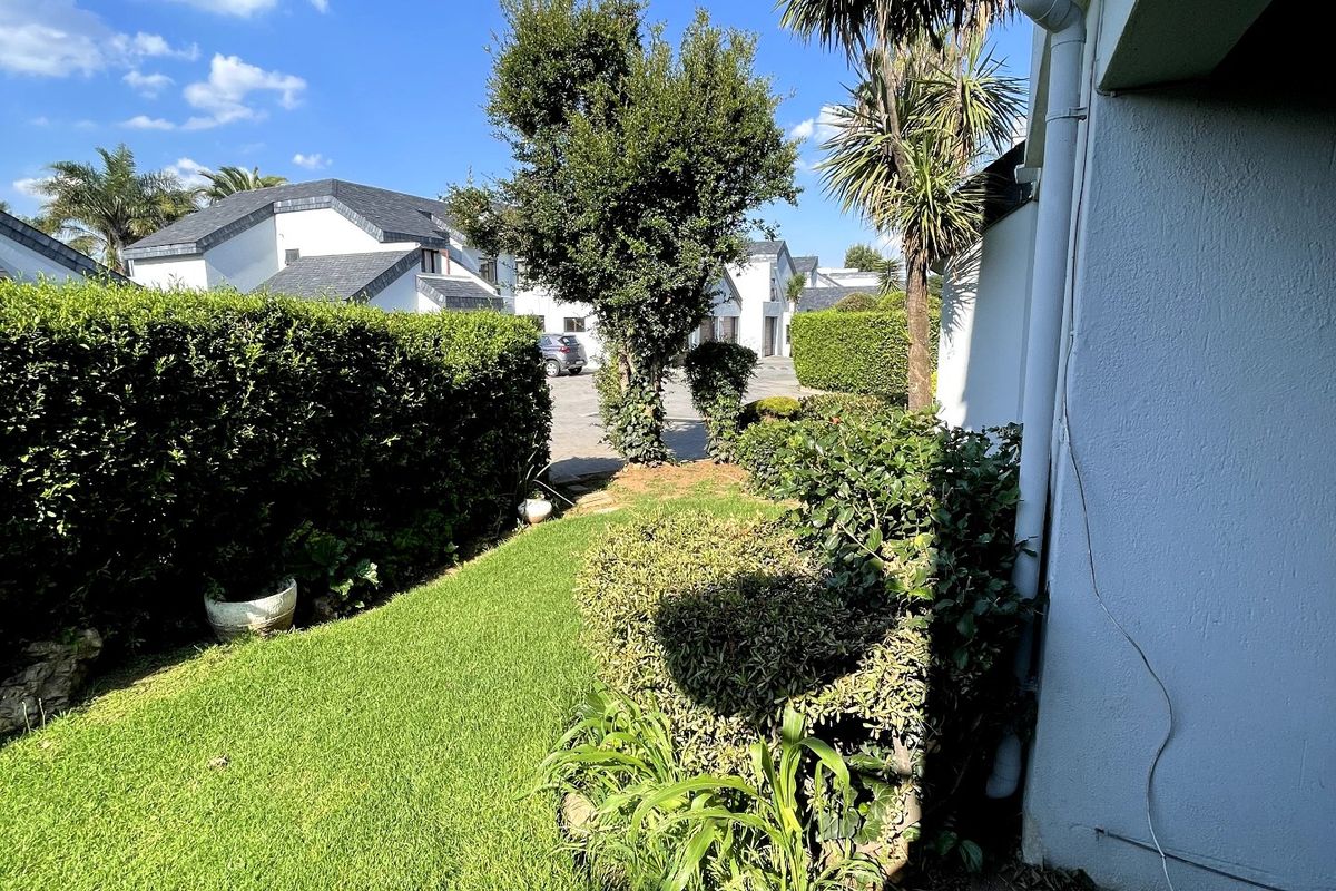 A well-maintained private garden area featuring a manicured lawn, established hedges, and a paved walkway adjacent to the townhouse exterior.