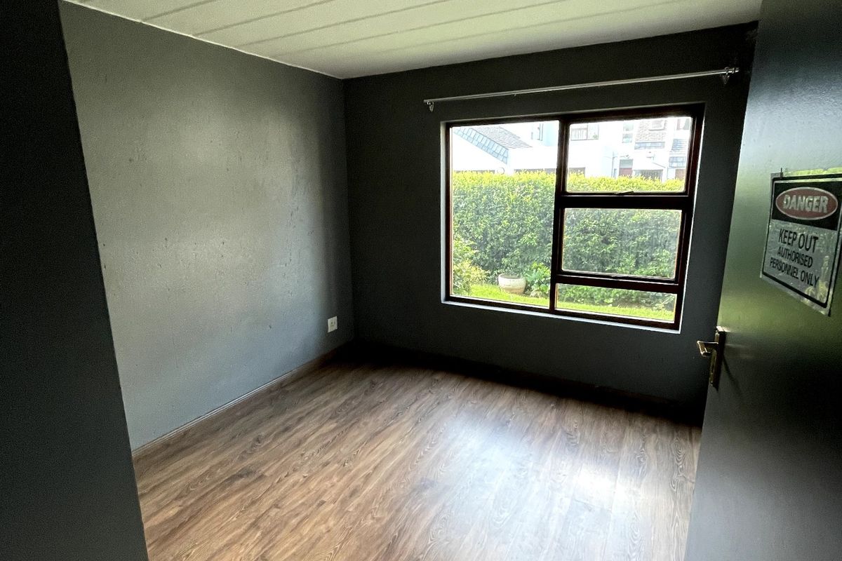 An empty bedroom featuring dark painted walls, wood-look laminate flooring, and a large aluminium-framed window overlooking the garden.