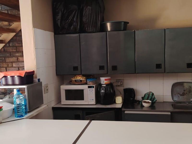 A functional kitchen area featuring built-in cabinetry, a stainless steel sink, and a tiled backsplash, adjacent to an exposed brick staircase.