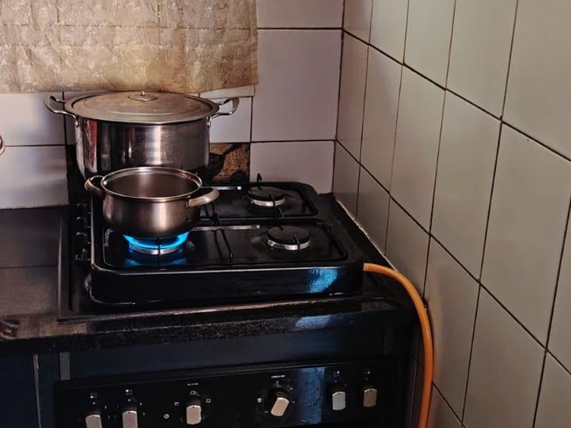 A compact kitchen area featuring a built-in oven, gas hob, and tiled splashback, requiring updates to finishes and gas installation safety.
