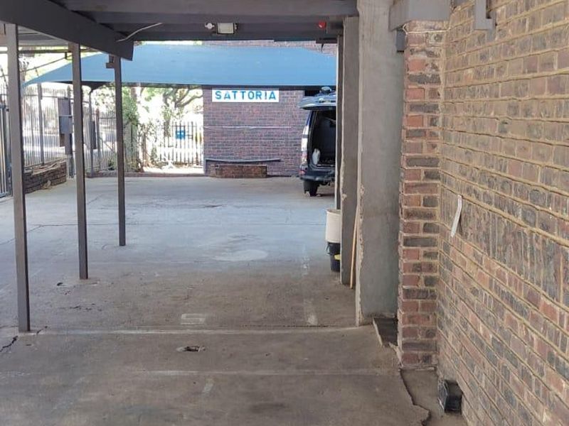 A covered outdoor parking area or carport featuring exposed brick walls, a corrugated metal roof, and concrete flooring.