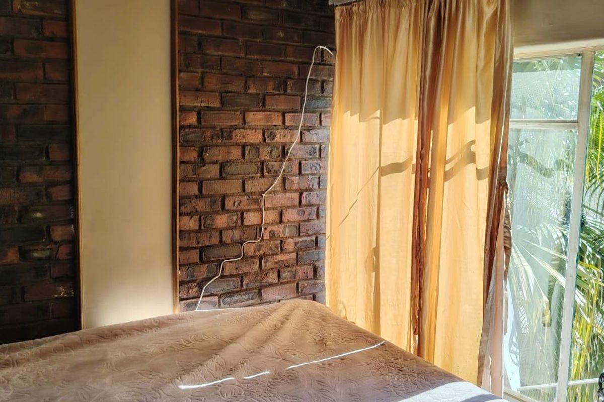 Bedroom featuring an exposed brick feature wall and large window providing natural light and garden views.