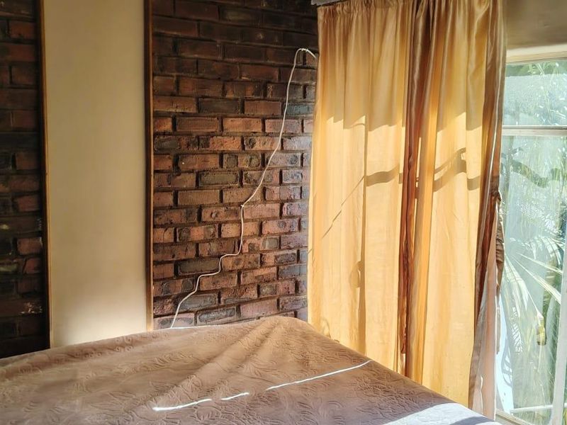 Bedroom featuring an exposed brick feature wall and large window providing natural light and garden views.