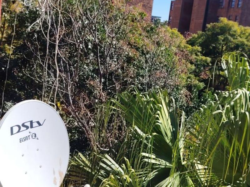 An outdoor view from the property looking towards neighboring apartment buildings, featuring a mounted satellite dish and surrounding greenery.