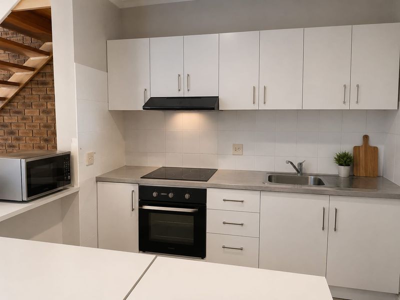 A clean, modern kitchen featuring white cabinetry, a built-in oven, electric cooktop, and a stainless steel sink with a tiled splashback.