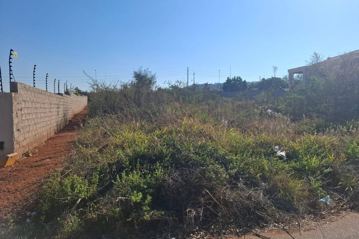 A vacant residential plot featuring a perimeter wall with electric fencing, currently covered in overgrown vegetation.