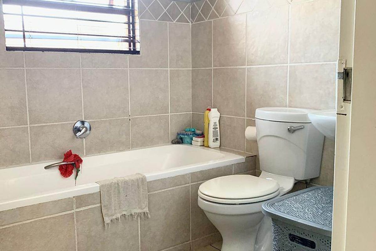 A functional bathroom featuring a bathtub, toilet, and pedestal basin with neutral wall and floor tiling.
