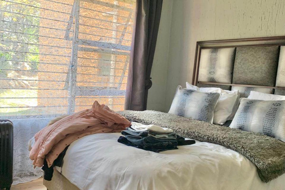 A well-lit bedroom featuring laminate flooring, textured wall finishes, and a large window allowing for natural light.