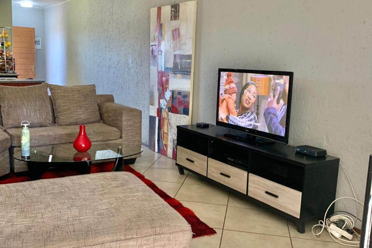 A living room area featuring tiled flooring and textured wall finishes, providing a functional space with an open-plan layout leading to the kitchen.