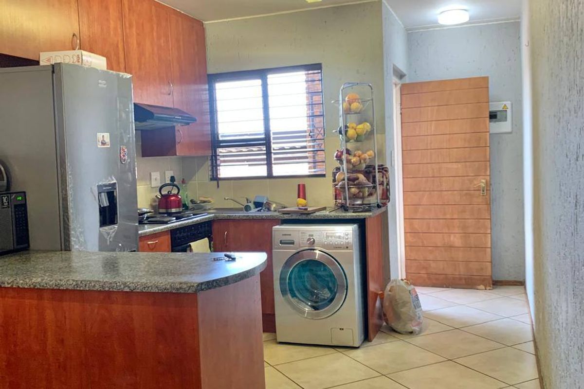 Functional kitchen featuring laminate cabinetry, granite countertops, built-in oven, hob, and tiled flooring with an integrated laundry appliance space.