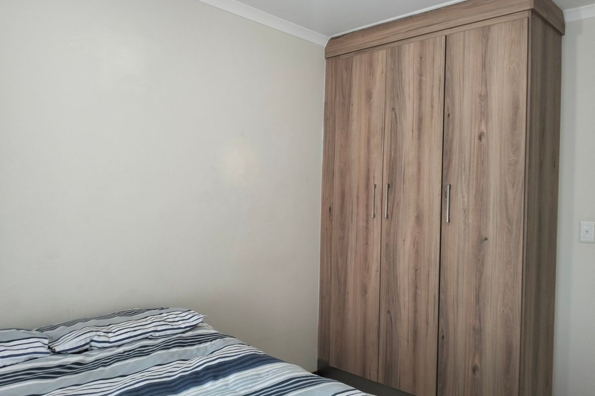 A bedroom featuring a modern wood-grain built-in wardrobe with ample storage space.