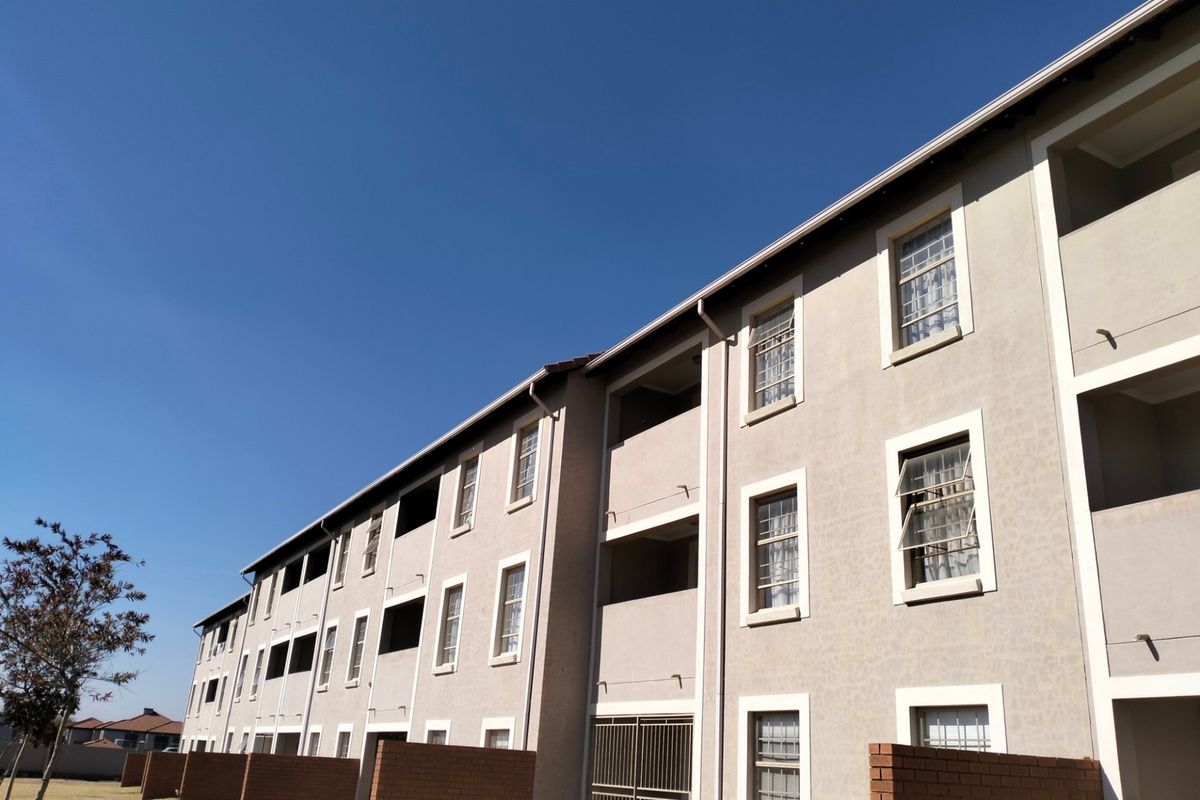 Exterior view of a multi-story apartment building featuring brick privacy walls, metal security gates, and standard casement windows.