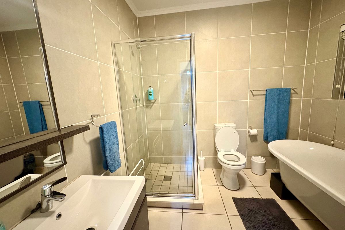 Modern bathroom featuring a glass shower enclosure, a freestanding bathtub, a vanity basin, and neutral floor-to-ceiling wall tiles.