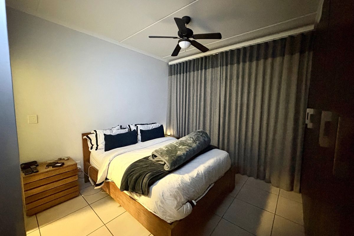 A functional bedroom featuring tiled flooring, a ceiling fan, and a built-in wardrobe, offering a comfortable and practical living space.