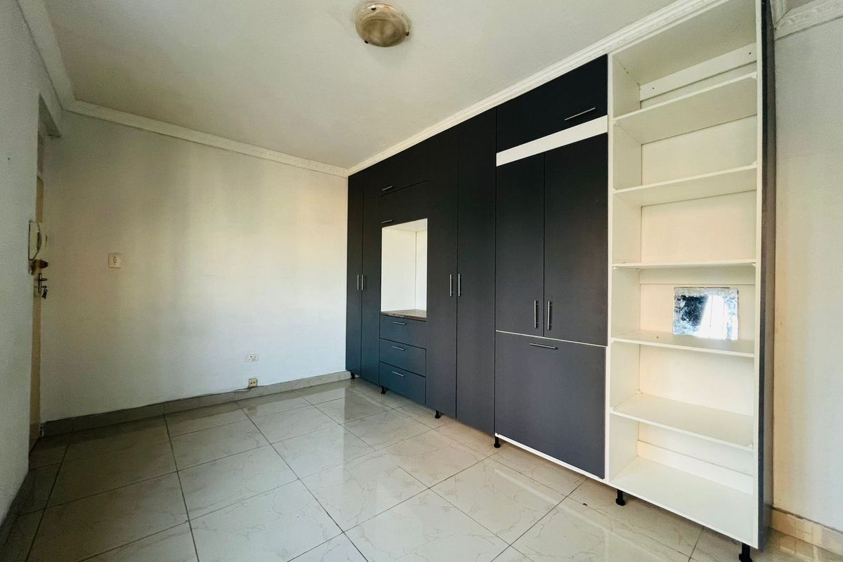 A vacant bedroom featuring large dark-toned built-in cupboards with integrated shelving and polished tile flooring.