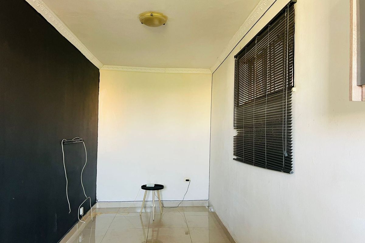 An empty living area featuring tiled flooring, a contrasting black accent wall, and venetian blinds, offering a blank canvas for personalization.
