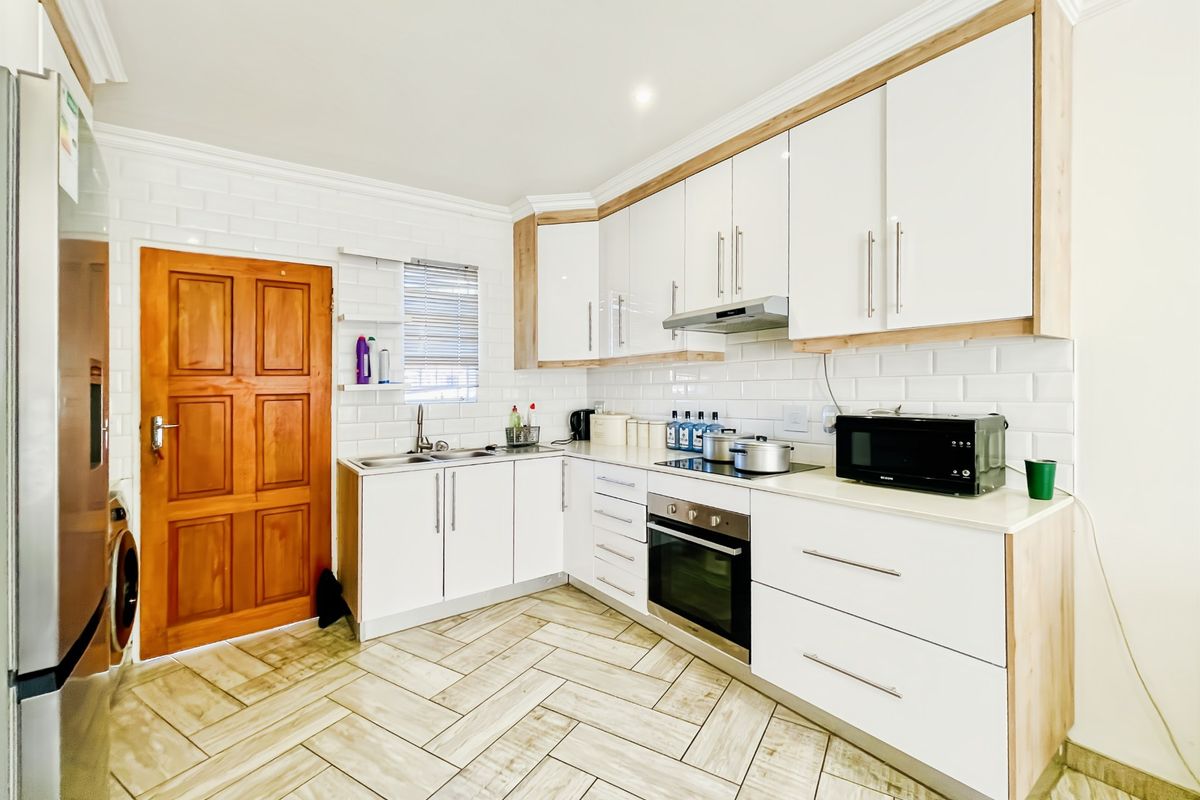 Modern kitchen featuring white cabinetry with wood-tone accents, subway tile backsplash, built-in oven, electric hob, and stylish herringbone tile flooring.