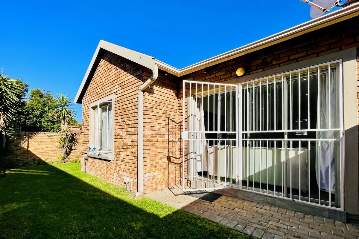 Rear view of the townhouse featuring a face brick facade, paved patio area, and secure sliding door access to the interior.