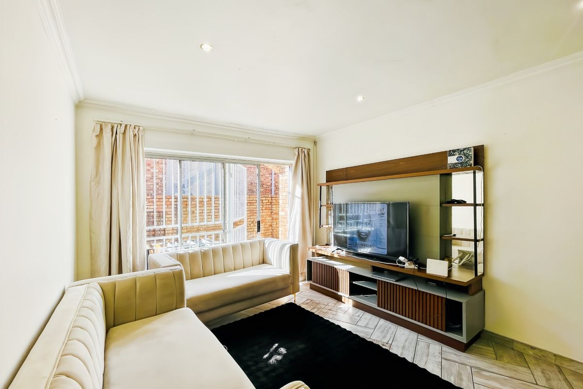 A bright and well-maintained living room featuring tiled flooring, recessed downlights, and a large sliding glass door providing natural light.