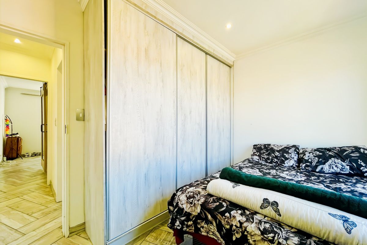A well-maintained bedroom featuring built-in sliding door wardrobes, recessed downlighting, crown molding, and tiled flooring, with a view into the adjacent hallway.