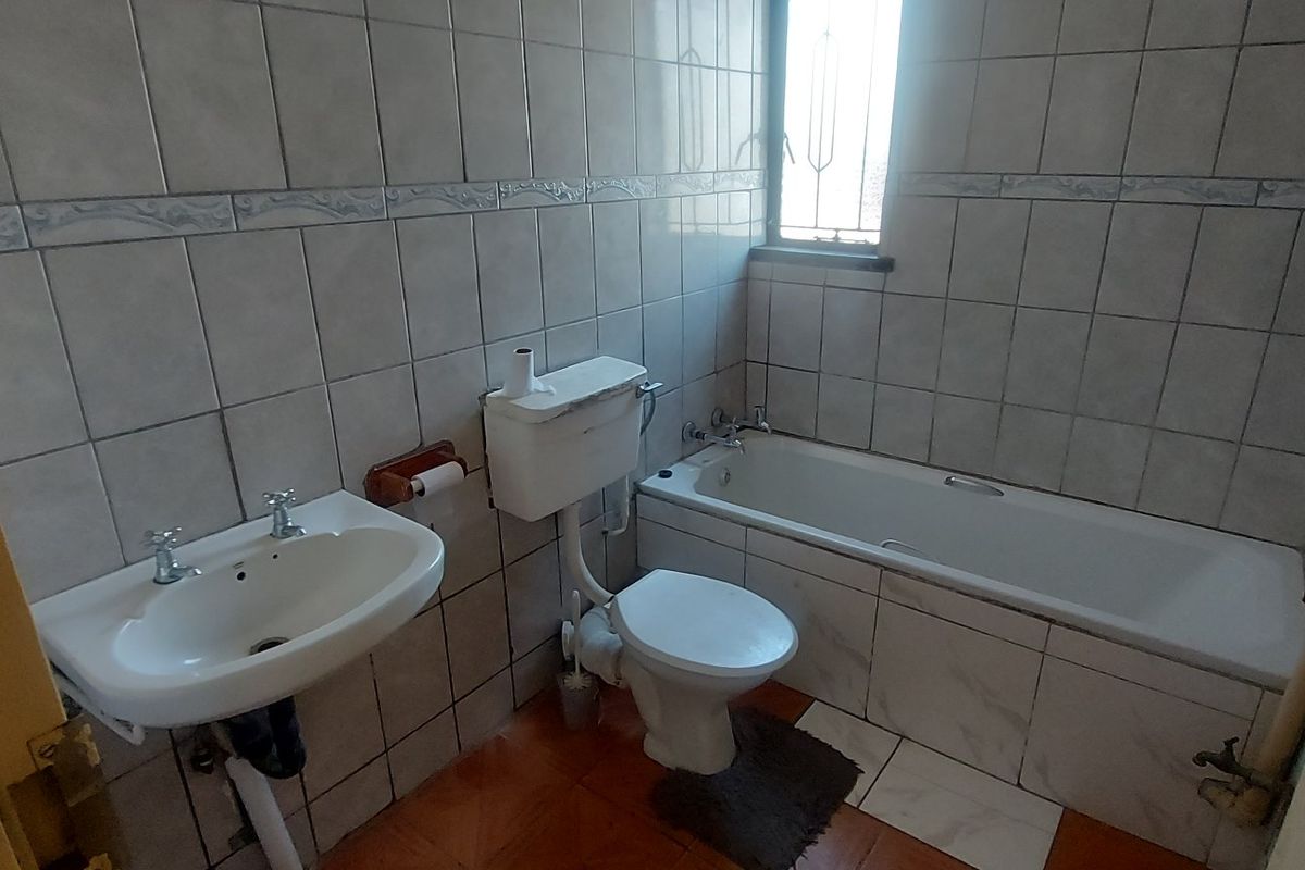 A functional bathroom featuring a bathtub, pedestal basin, and toilet, finished with full-height wall tiling and tiled flooring.
