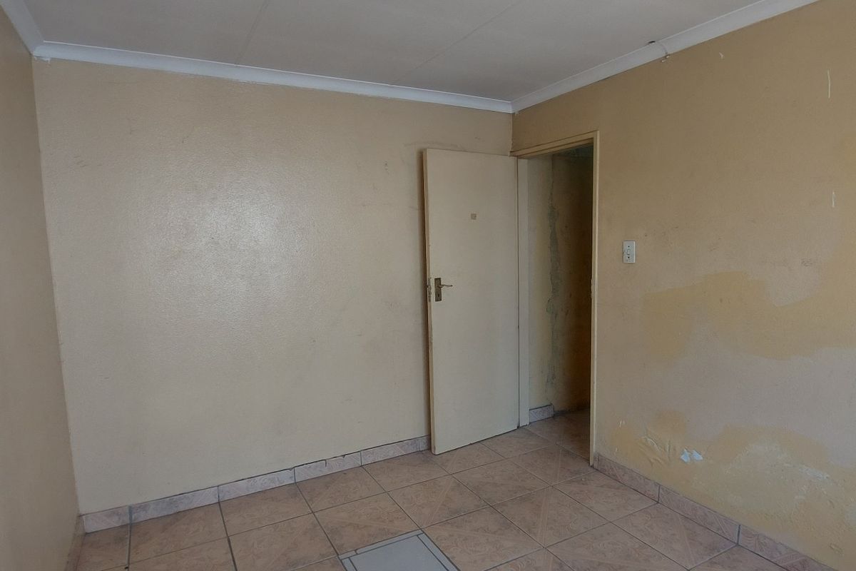 An empty bedroom featuring tiled flooring and plain walls, currently requiring cosmetic updates and repairs to the wall finishes.