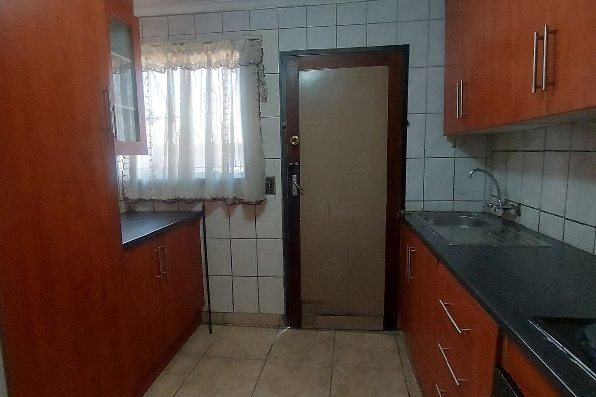 A functional kitchen featuring laminate cabinetry, dark countertops, tiled backsplash, and tiled flooring, offering a dated aesthetic ready for modernization.