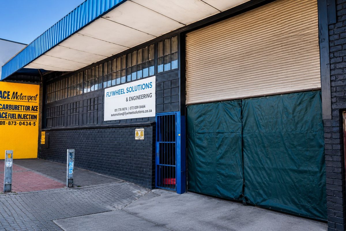 Commercial industrial unit facade featuring a large roller shutter door, security gate, and prominent signage for business visibility.