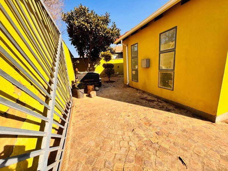 A side exterior view of the property featuring paved ground, yellow exterior walls, and metal security gate access.