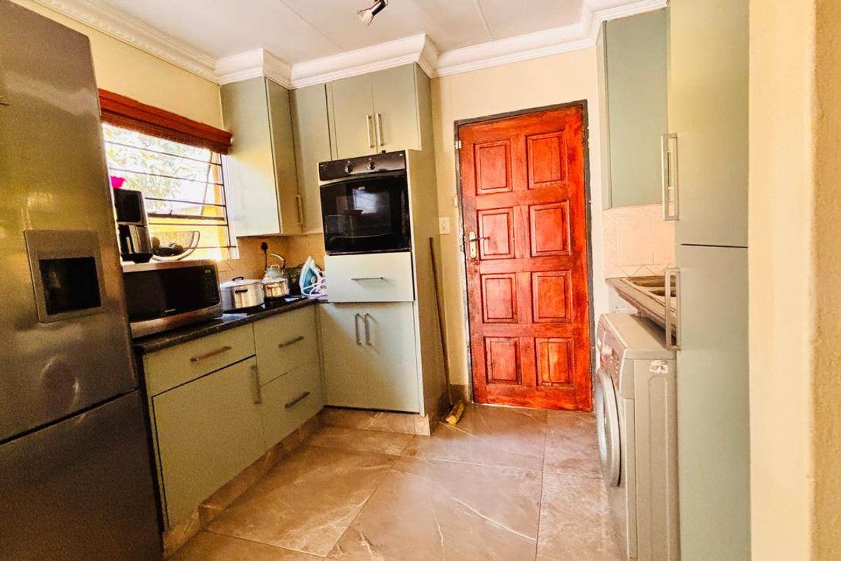 A functional kitchen featuring built-in cabinetry, a wall-mounted oven, and tiled flooring, providing a practical workspace with direct access to an exterior door.