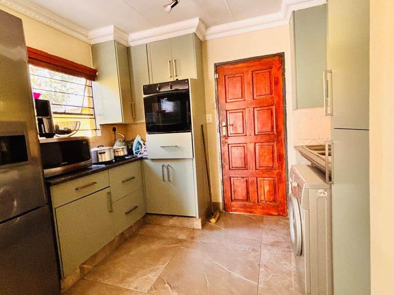A functional kitchen featuring built-in cabinetry, a wall-mounted oven, and tiled flooring, providing a practical workspace with direct access to an exterior door.