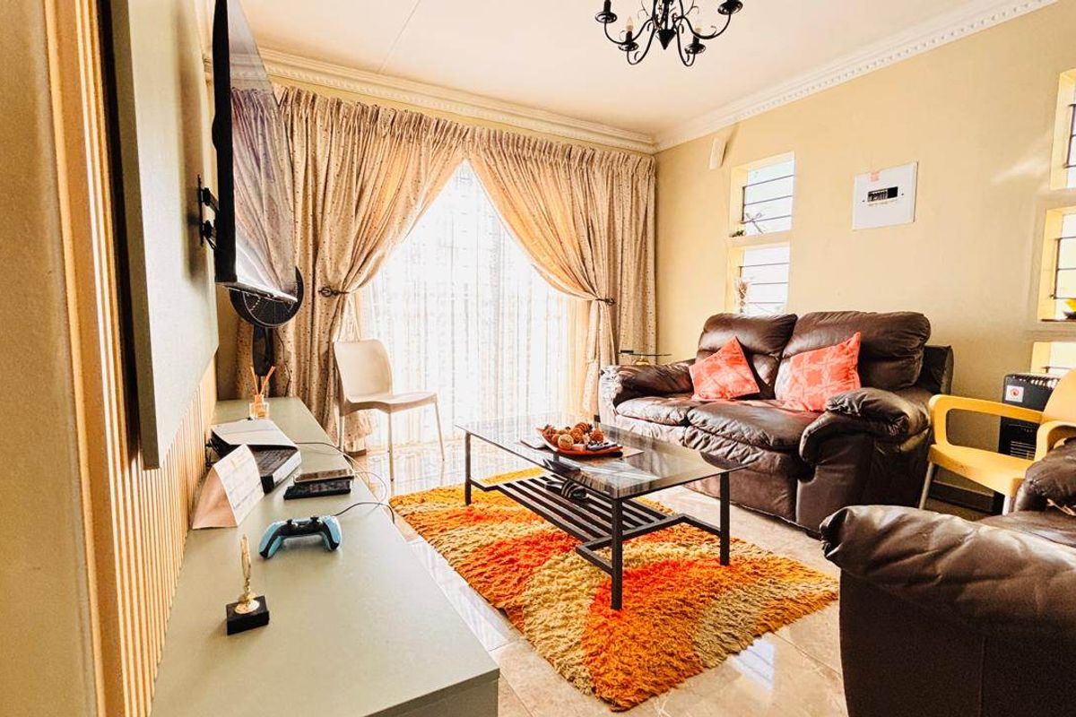 A comfortable living room featuring tiled flooring, a coved ceiling with a chandelier, and a sliding glass door providing natural light.