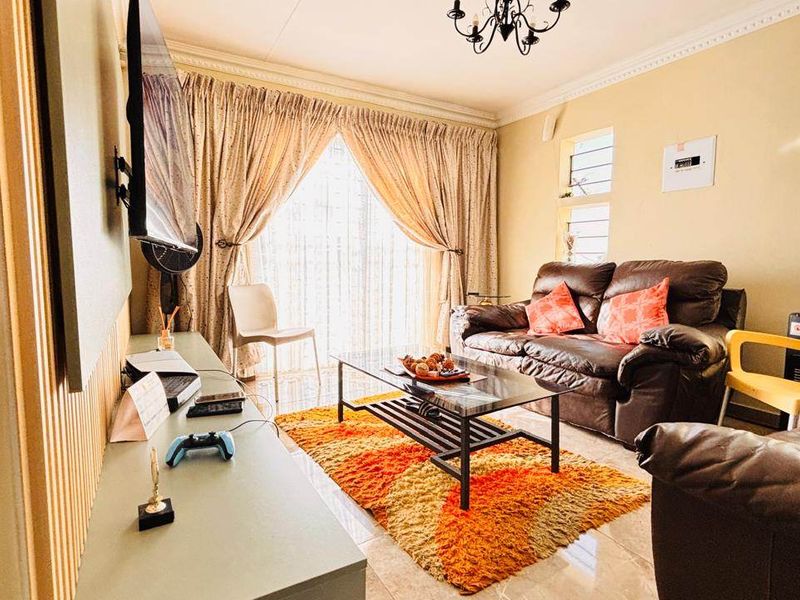 A comfortable living room featuring tiled flooring, a coved ceiling with a chandelier, and a sliding glass door providing natural light.