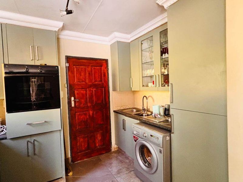 A functional scullery area featuring sage green cabinetry, integrated oven, stainless steel sink, and tiled flooring, providing additional prep and utility space.