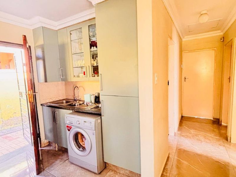 A functional laundry area featuring built-in cabinetry, a stainless steel sink, and tiled flooring, with direct access to an outdoor space.
