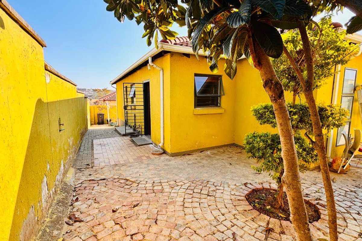 A rear exterior view of the property featuring a paved courtyard, security gate, and yellow painted exterior walls with some visible wear.