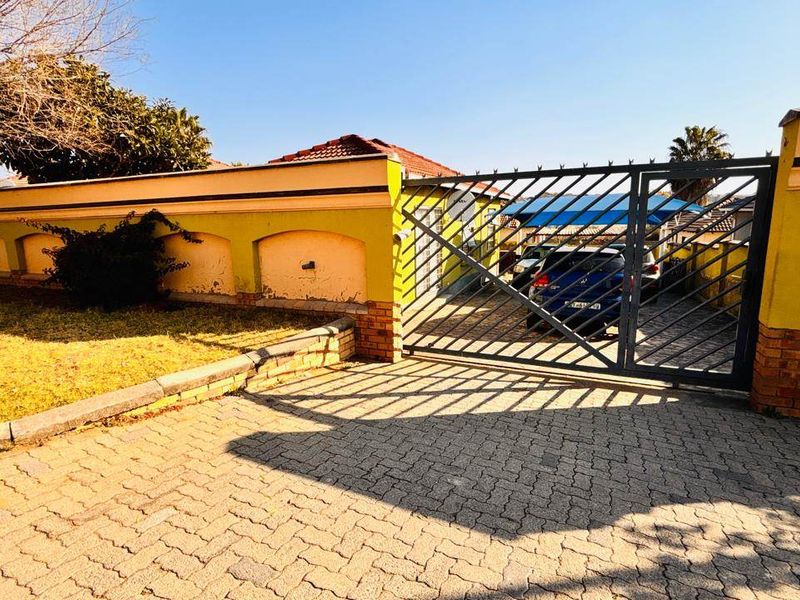 Front exterior view of the property featuring a paved driveway, metal security gate, and perimeter wall with integrated lighting.