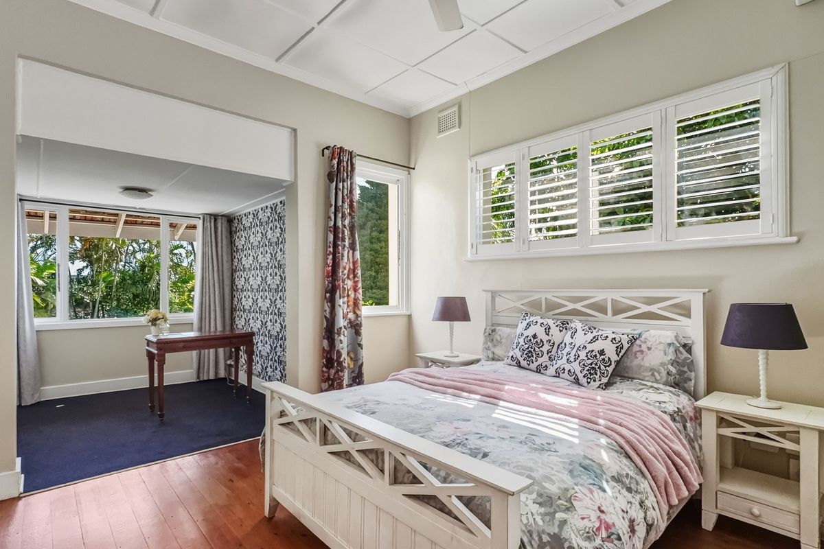 A bright bedroom featuring polished timber flooring, plantation shutters, and a coffered ceiling, with an adjoining study or sitting area.