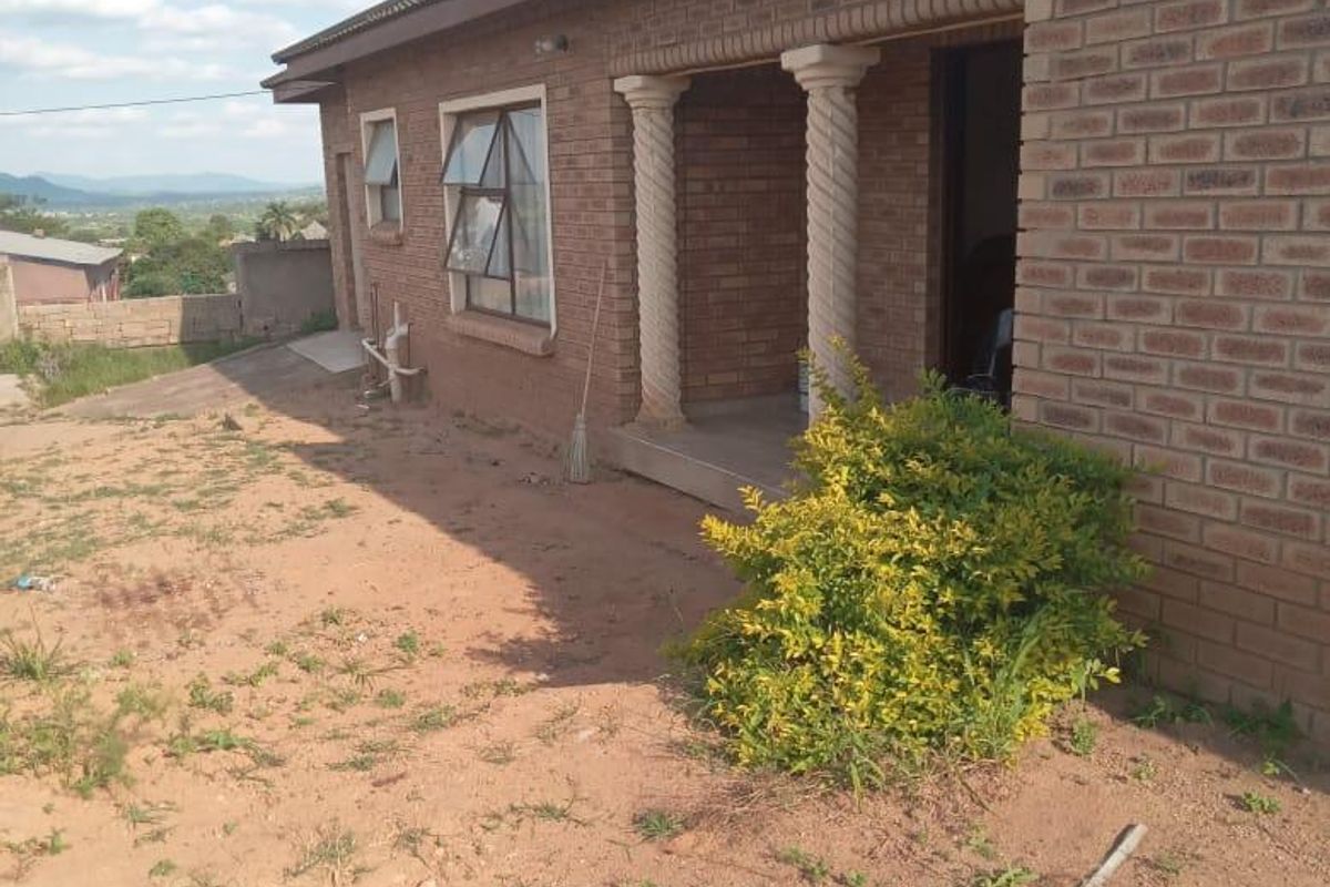 Rear view of a face brick house featuring decorative columns and a covered patio area, set on an unlandscaped plot.