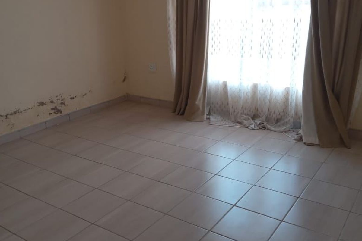 An empty bedroom featuring tiled flooring and natural light, currently requiring wall repairs and cosmetic updates.
