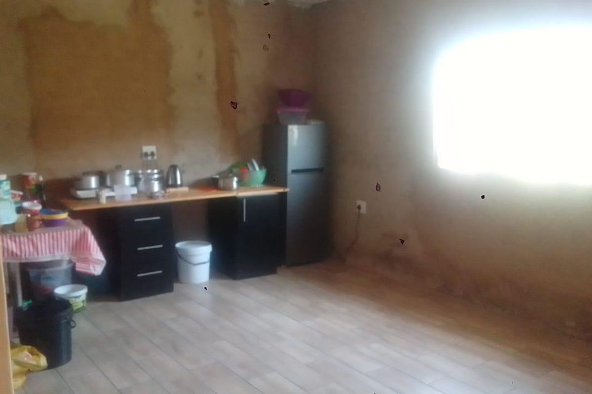 A basic kitchen area featuring laminate flooring and minimal cabinetry, currently requiring significant wall repairs and cosmetic updates to improve the overall condition.